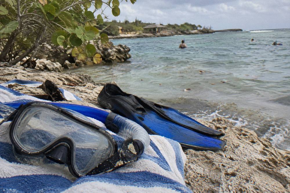 A snorkel mask and fins laid out on a beach towel beside a calm bay