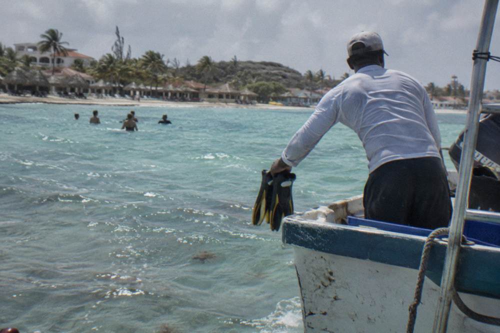 A crew member handing snorkel fins to guests at the stern of a boat