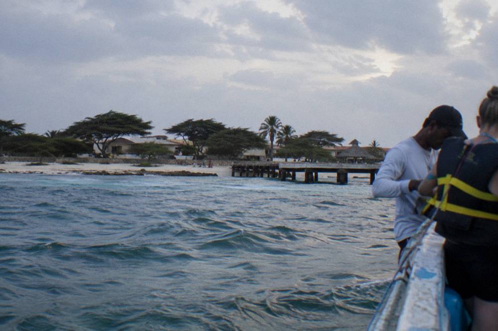 Guide fitting a snorkel vest on a guest beside a small boat at a beach pier