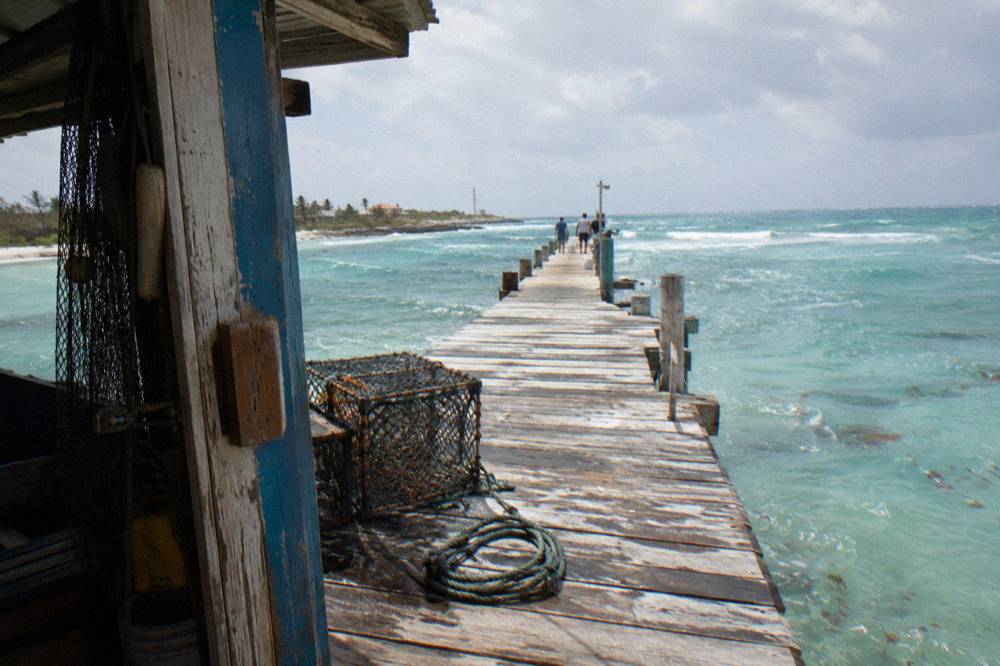 A wooden fishermen's pier extending over shallow turquoise water toward open sea