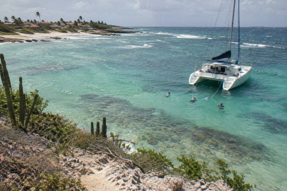 A catamaran moored near a shallow reef with snorkelers in the water beside it