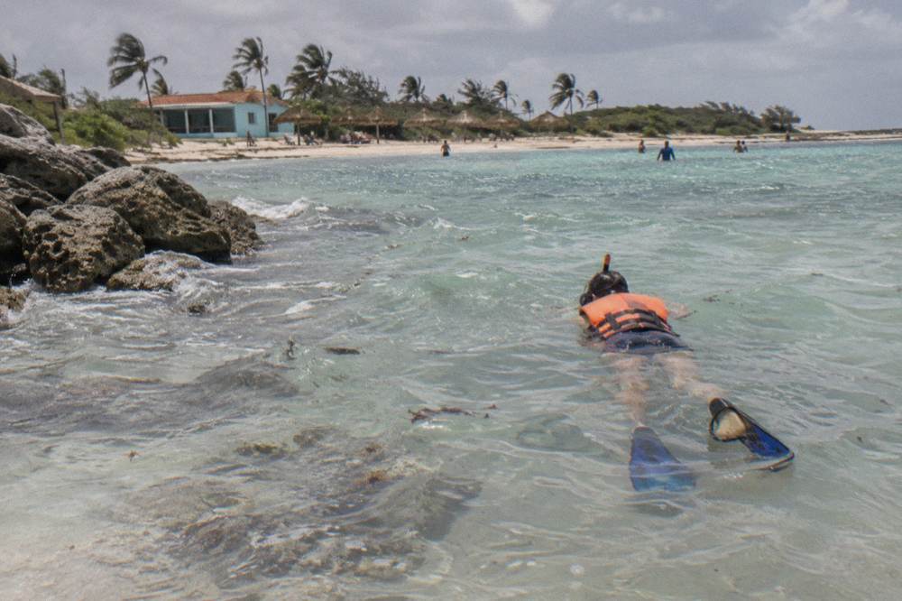 A person in a life jacket floating face down over a quiet sandy-bottom bay