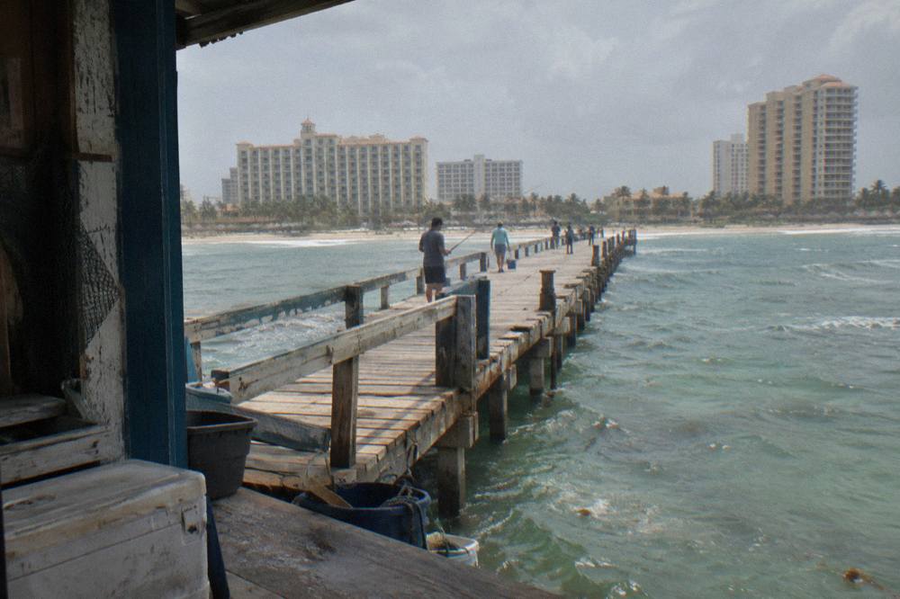 A wooden pier extending over calm green water with hotel towers along the shore