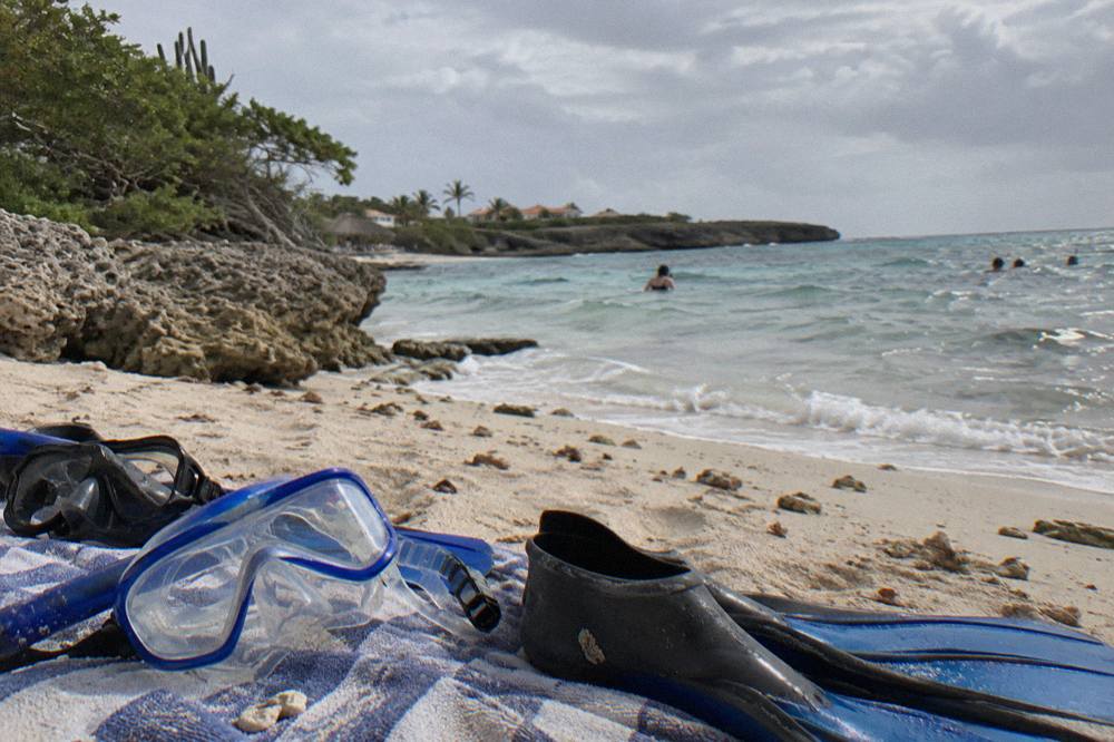 Children's snorkel masks and fins laid out on a beach towel beside a calm bay