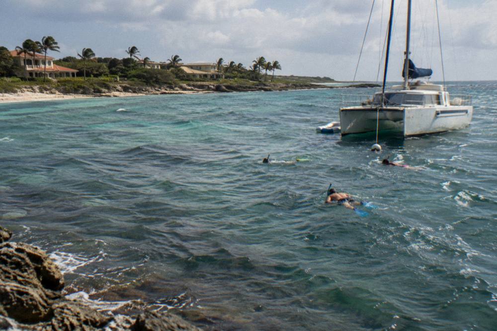A catamaran anchored near a shallow reef with snorkelers in the water