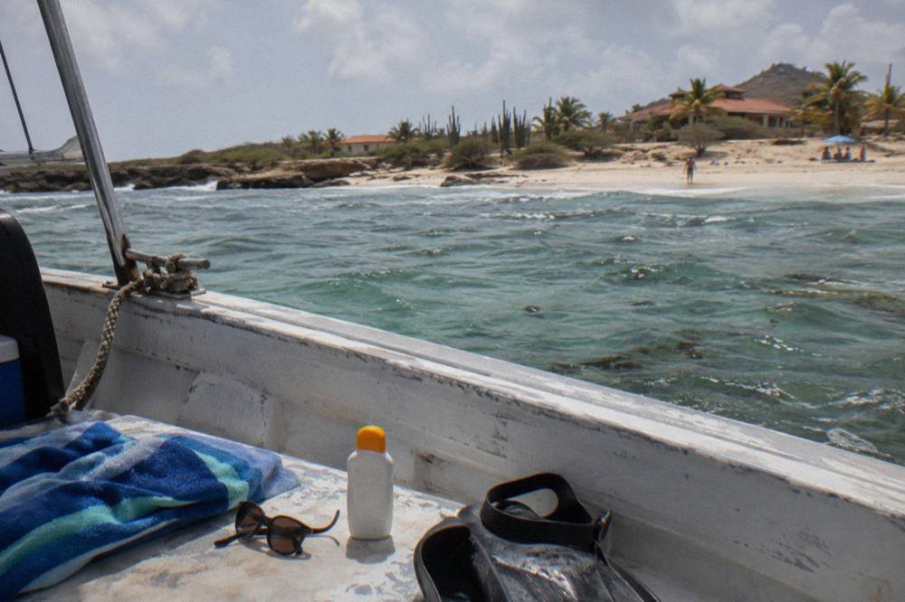 A folded towel, sunglasses and a bottle of mineral sunscreen arranged on a boat deck bench