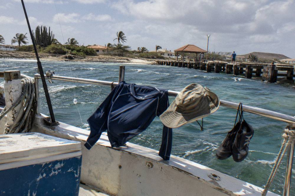 A rash guard, water sandals and a wide-brimmed hat drying on the railing of a small boat