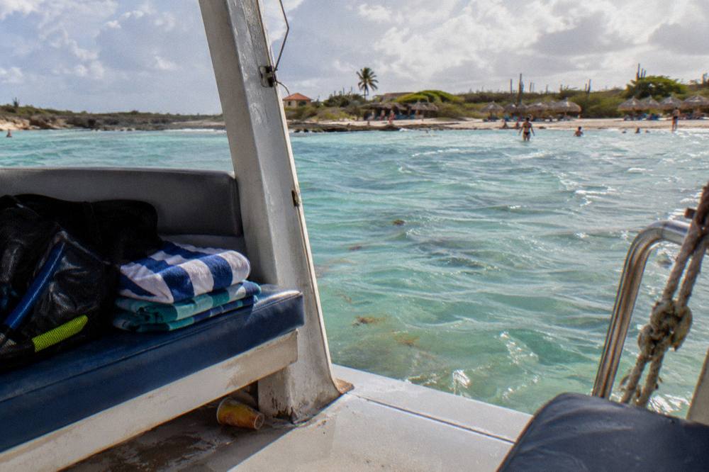 A shaded bench on a small boat with a stack of folded towels and a mesh bag of snorkel gear